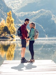 Verliebtes Paar auf einem Holzsteg am See mit bewaldeten Bergen im Hintergrund