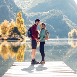 Verliebtes Paar auf einem Holzsteg am See mit bewaldeten Bergen im Hintergrund