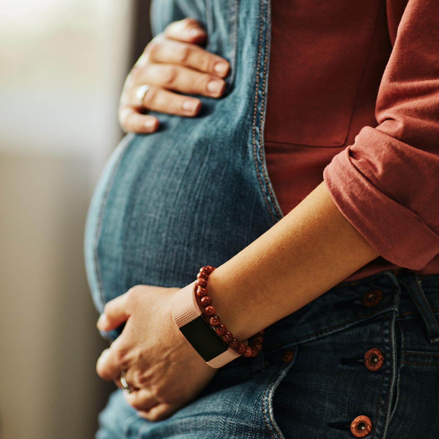 Eine schwangere Frau hält behutsam die Hände auf ihren Bauch und trägt eine Jeans Latzhose