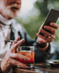 Älterer Mann mit Smartphone, Whisky und Zigarette