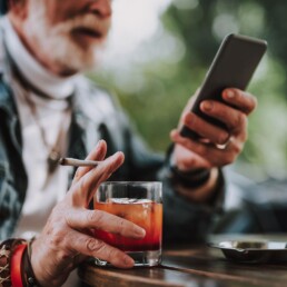 &Auml;lterer Mann mit Smartphone, Whisky und Zigarette