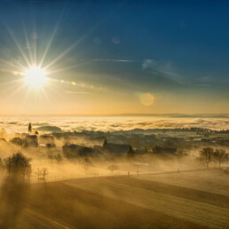 Die Sonne geht im Winter &uuml;ber einem Nebelbedeckten Dorf auf
