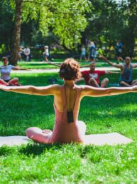 Yogalehrerin unterrichtet Yoga im Park auf einer grünen Wiese unter vereinzelten Bäumen