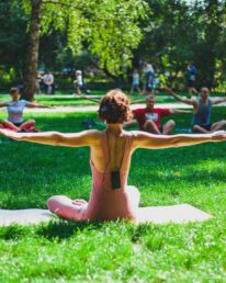 Yogalehrerin unterrichtet Yoga im Park auf einer grünen Wiese unter vereinzelten Bäumen