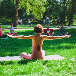 Yogalehrerin unterrichtet Yoga im Park auf einer gr&uuml;nen Wiese unter vereinzelten B&auml;umen